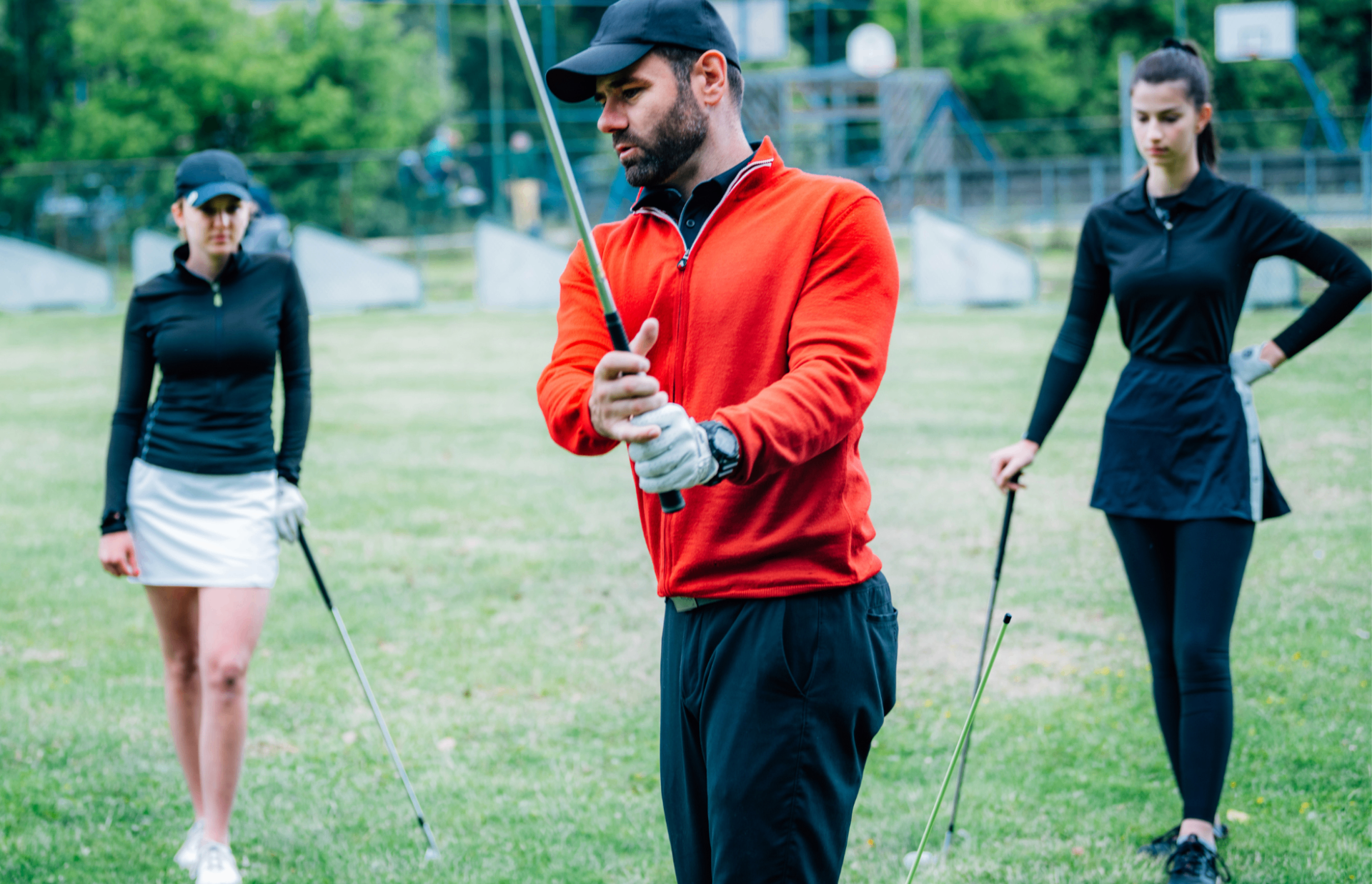 A golfer in a red pullover demonstrating a swing with two golfers watching.