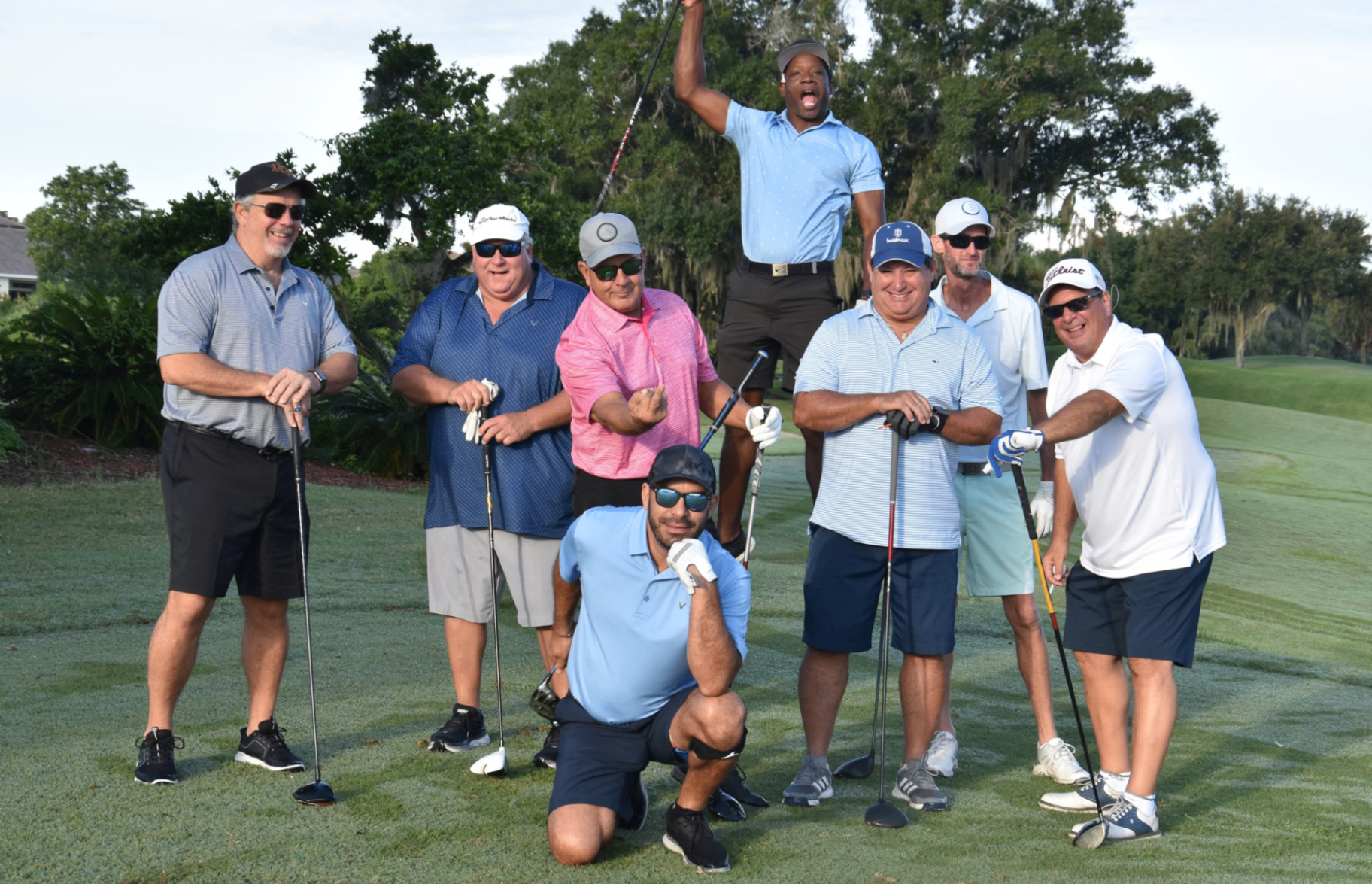 A group of golfers posing playfully together on a fairway with clubs in hand.