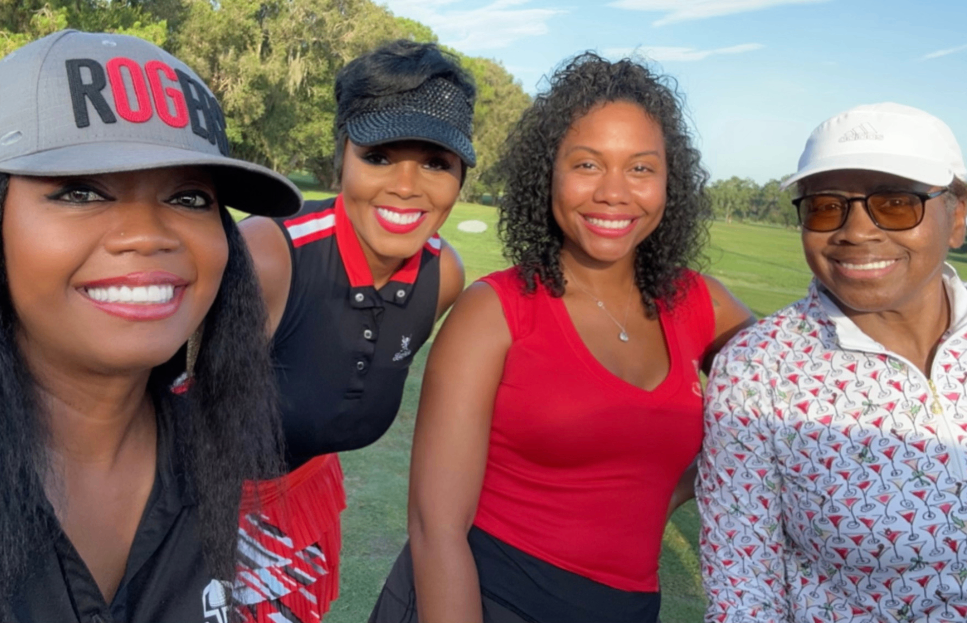 Four golfers smiling together on the course in black, red, and white outfits.